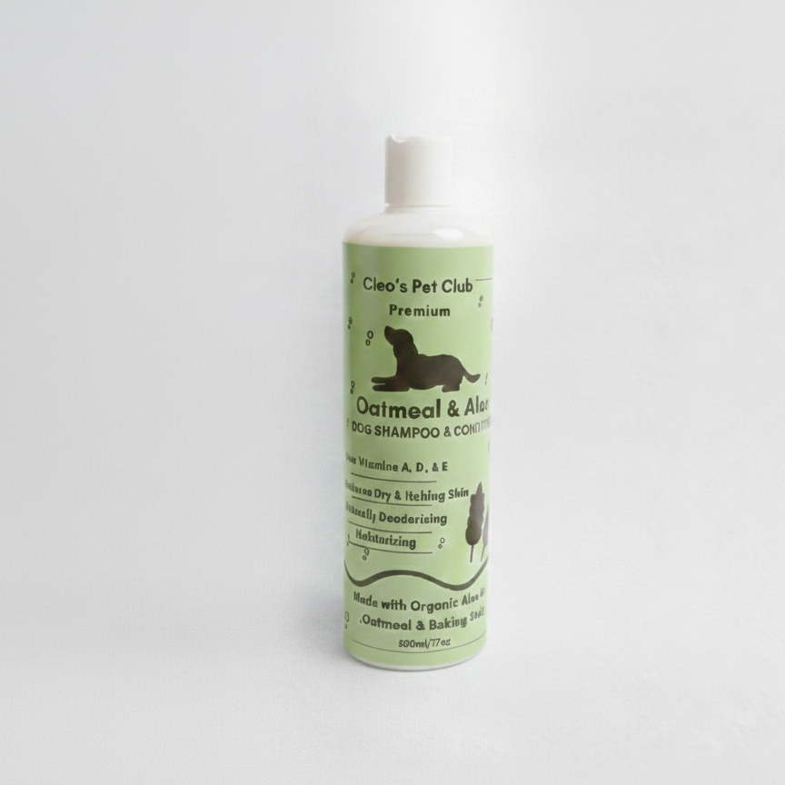 A square product mockup featuring a bottle of Cleo's Pet Club Oatmeal and Aloe Dog Shampoo next to a matching grooming brush with a small amount of foam on the bristles. The bottle has a light green label with a dog silhouette, all set against a clean, light gray background.